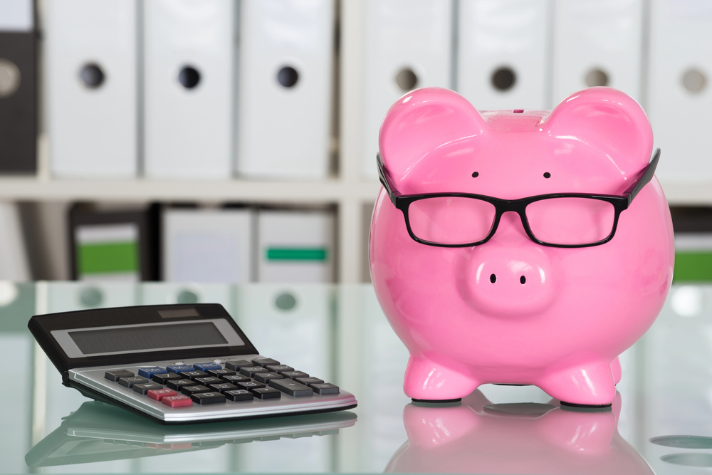 pink piggy bank with glasses on a glass table with a calculator to the left