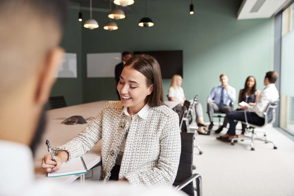 woman sitting at a desk smiling while writing in a notebook